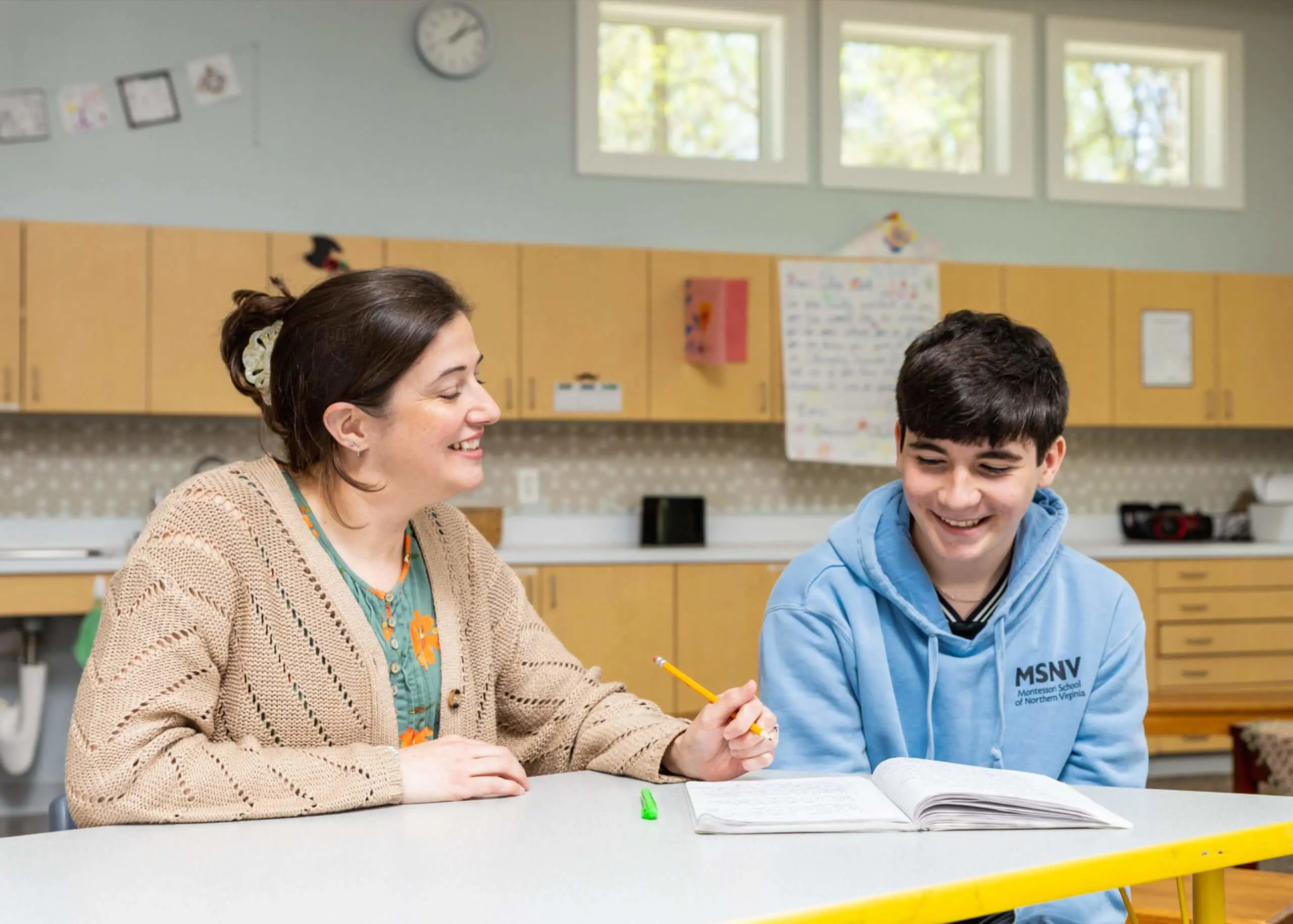 An MSNV Middle School teacher and student reviewing work together at a classroom table.