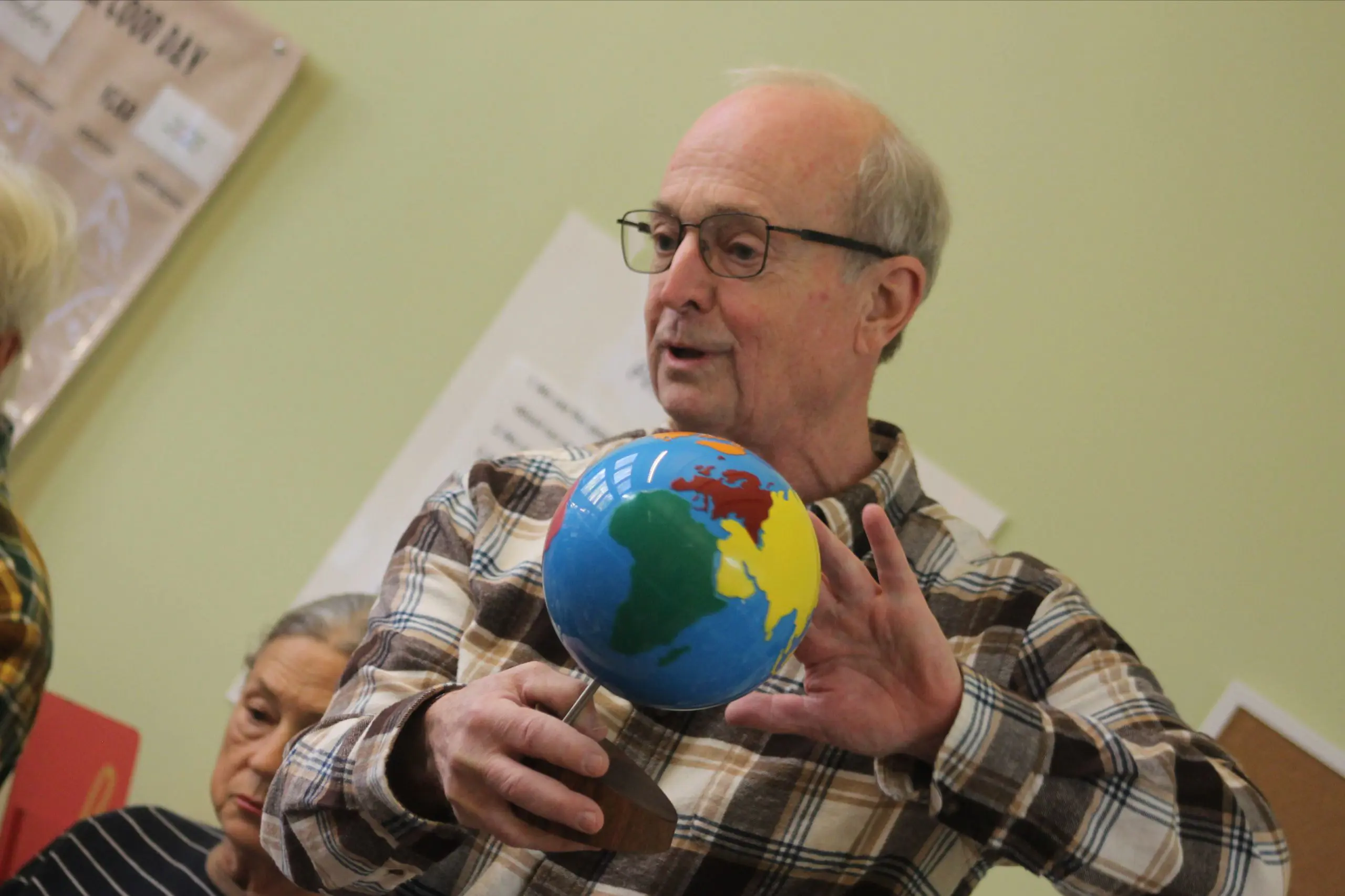 A grandparent holding a globe and engaging with students during a visit to an MSNV classroom.