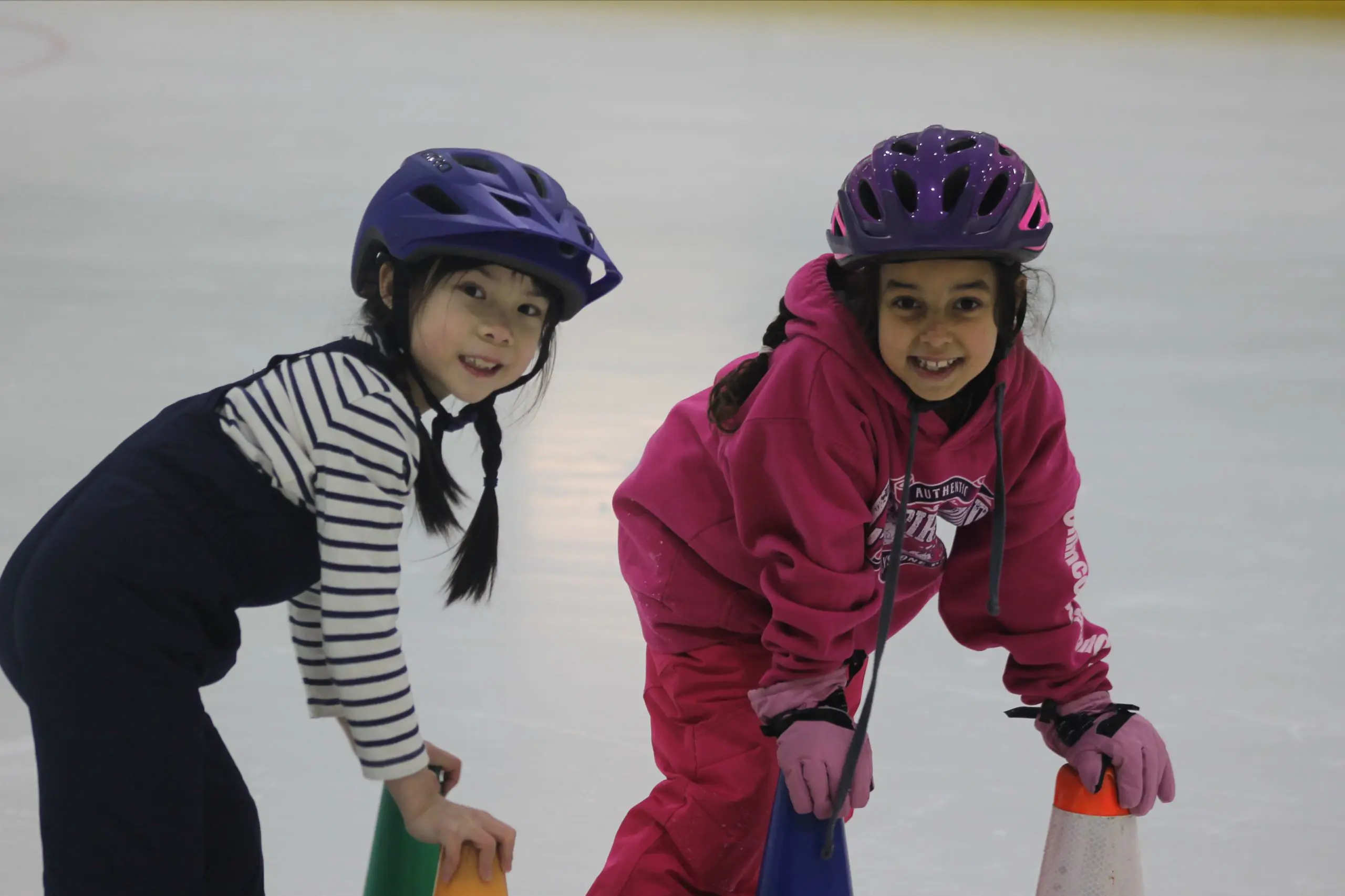 Two MSNV students in helmets skating together during a physical education ice skating activity.
