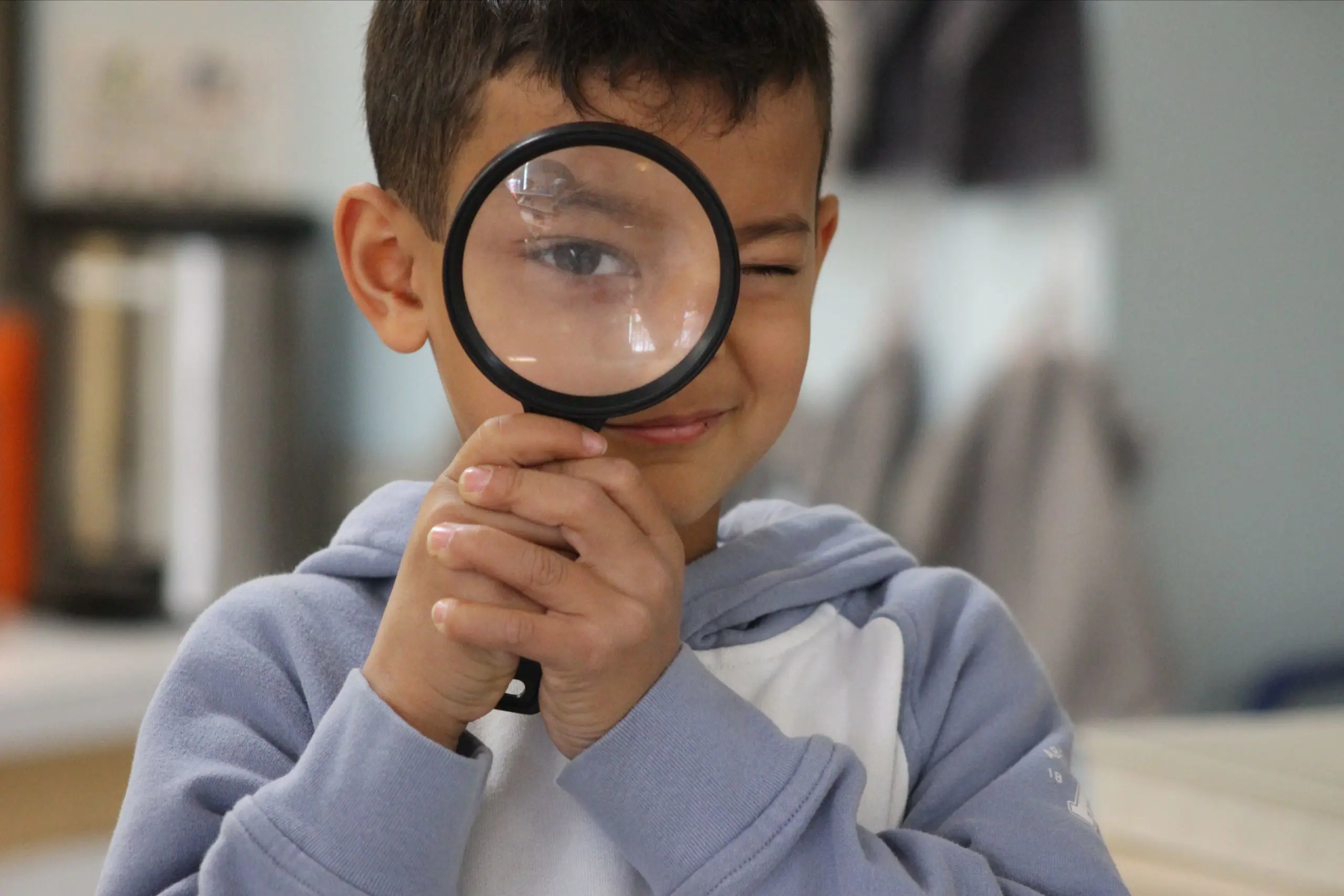 An MSNV elementary student looking through a magnifying glass with curiosity in a classroom setting.